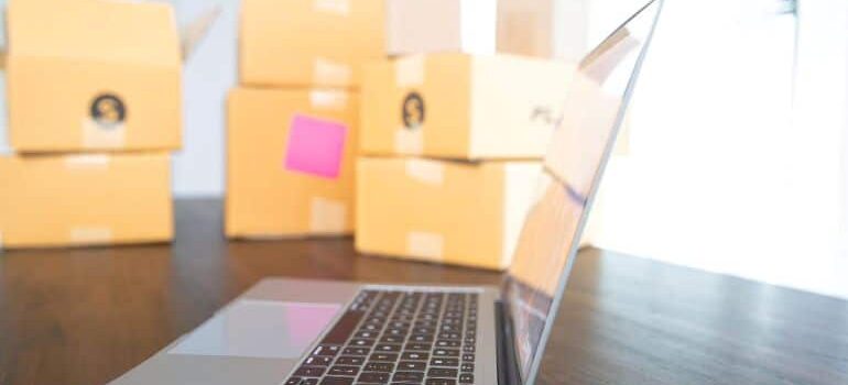 A laptop with a pile of cardboard moving boxes in the background.