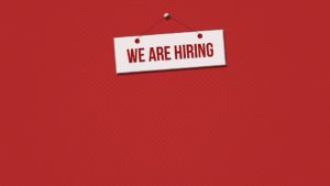 We Are Hiring sign in front of a red background.