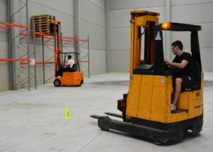 Two men driving forklifts in warehouse.