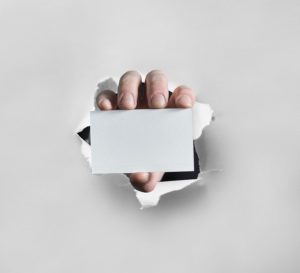 Hand with business card coming through a wall.