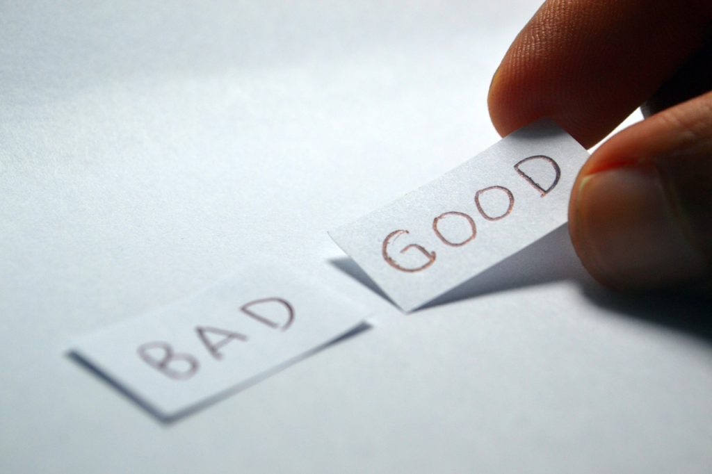 A hand picking a piece of paper with the word GOOD written on it. The word BAD on another piece of paper next to it.