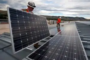 Workers placing solar panels on the top of a building.