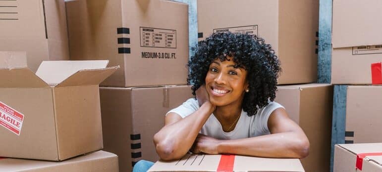 A happy woman sitting behind moving boxes and smiling.