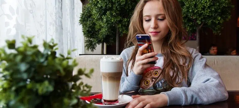 Girl at a coffee shop using her phone and being targeted by mobile marketing strategies for small businesses.