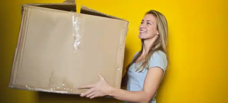 Woman carrying a large carboard box next to a yellow wall