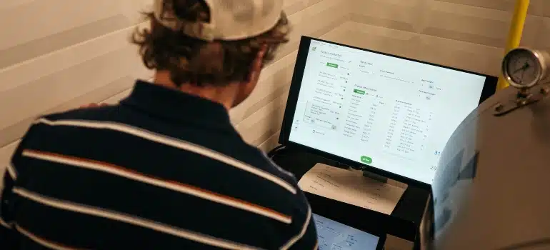 Man wearing a baseball cap sitting at a desk and analyzing data on their laptop