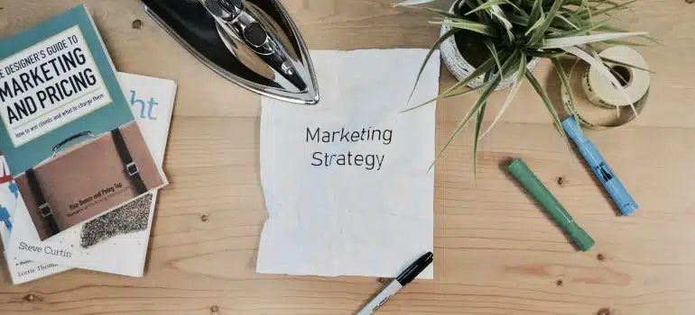 Paper with "Marketing strategy" printed on it between pens and a book