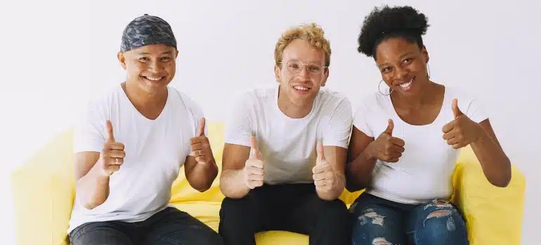 Three people sitting on a yellow couch and holding thumbs up