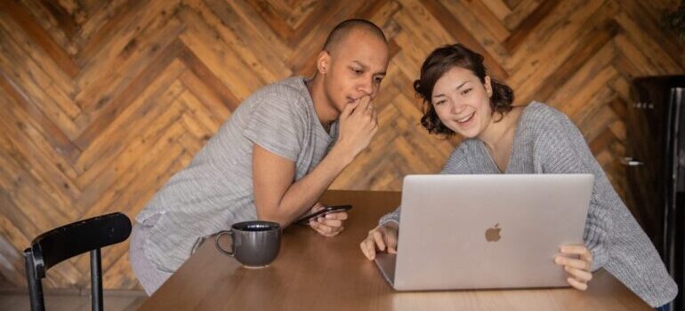 Two people sitting at a table and researching email marketing best practices for long distance moving companies on a laptop