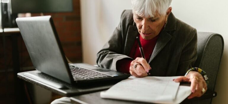 Elderly woman taking notes from laptop into a notebook