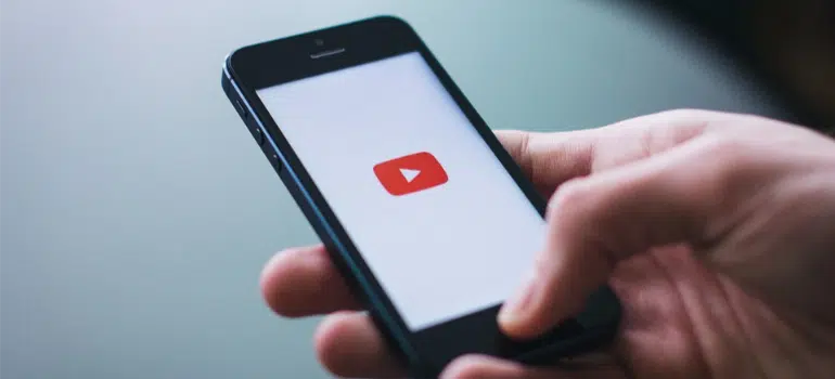 A person holding a smartphone that displays the YouTube logo.
