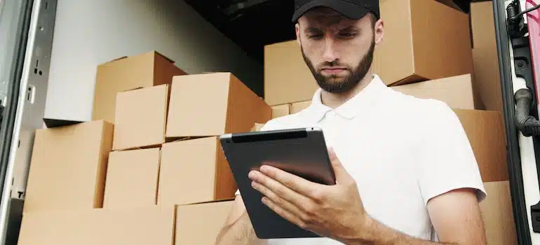a man standing in front of moving boxes and checking his notepad
