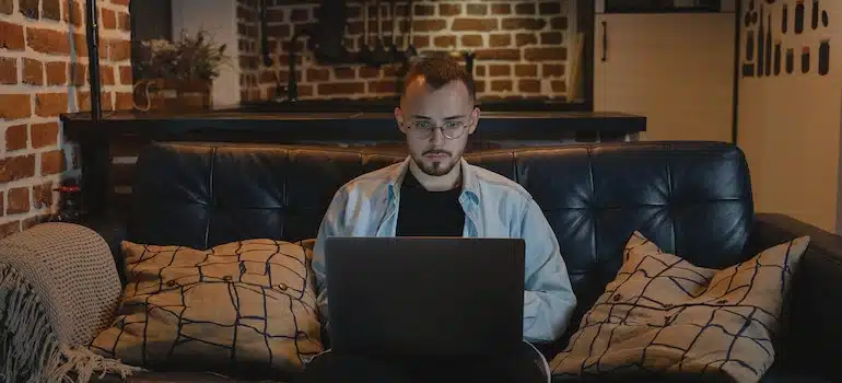 man working from home sitting on his couch with a laptop on this lap