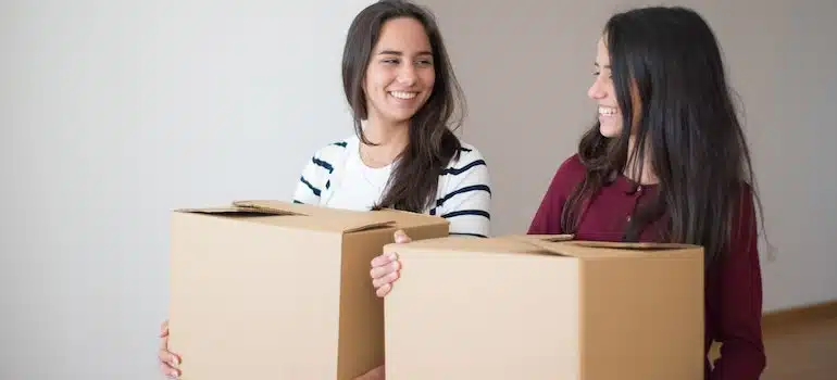 Two millennials carrying moving boxes and smiling.