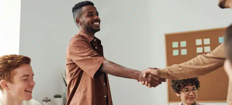 A smiling man shakes hands with a colleague, symbolizing the establishment of new referral partners for a moving company.