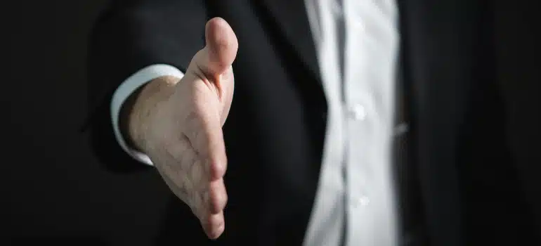 A person in a suit putting his hand forward to shake it. 