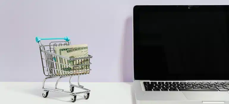 Shopping cart with money beside a laptop, illustrating using digital marketing to address customer objections.