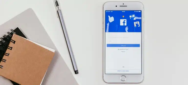 Smartphone displaying Facebook login screen next to a pen and notebook on a white desk.