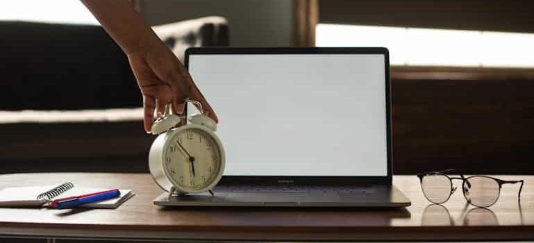 a hand holding an alarm clock in front of a laptop